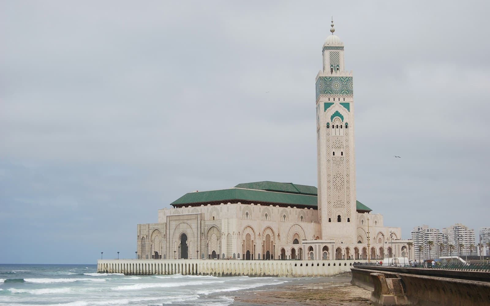 La mosquée Hassan II à Casablanca, son minaret décoré de zellige vert et sa terrasse au bord de l'océan Atlantique, sous un ciel nuageux