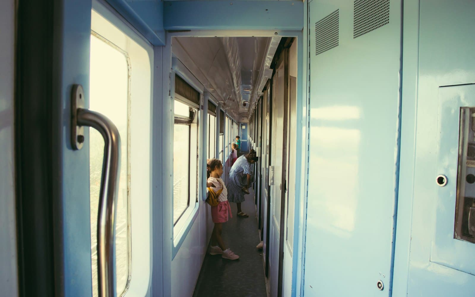 Couloir d'une voiture de train au Maroc, fenêtres ouvertes sur la voie, voyageurs au loin