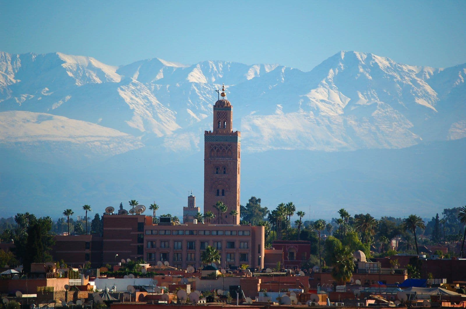 Le minaret de la Koutoubia à Marrakech, avec les sommets enneigés du Haut Atlas en arrière-plan et les toits de la ville au premier plan