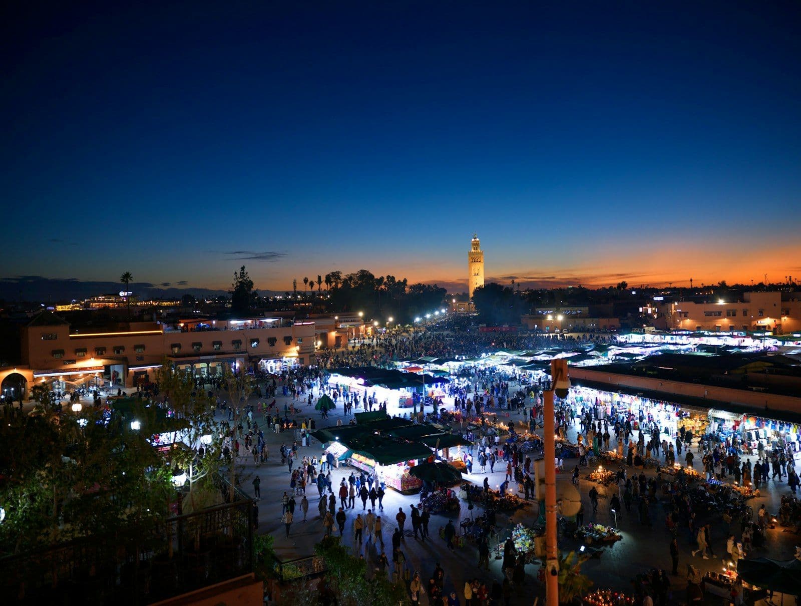 La place Jemaa el-Fna au crépuscule, avec ses étals illuminés et le minaret de la Koutoubia