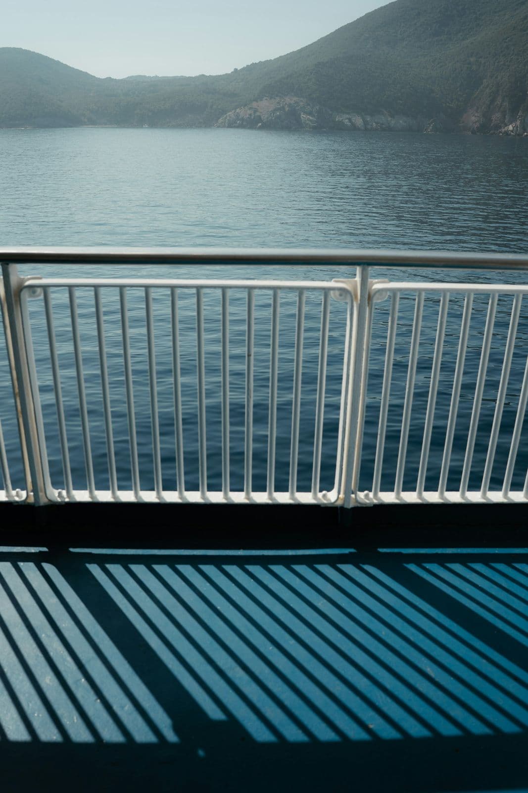 Pont d'un ferry avec sa rambarde blanche, la mer et une côte boisée en arrière-plan