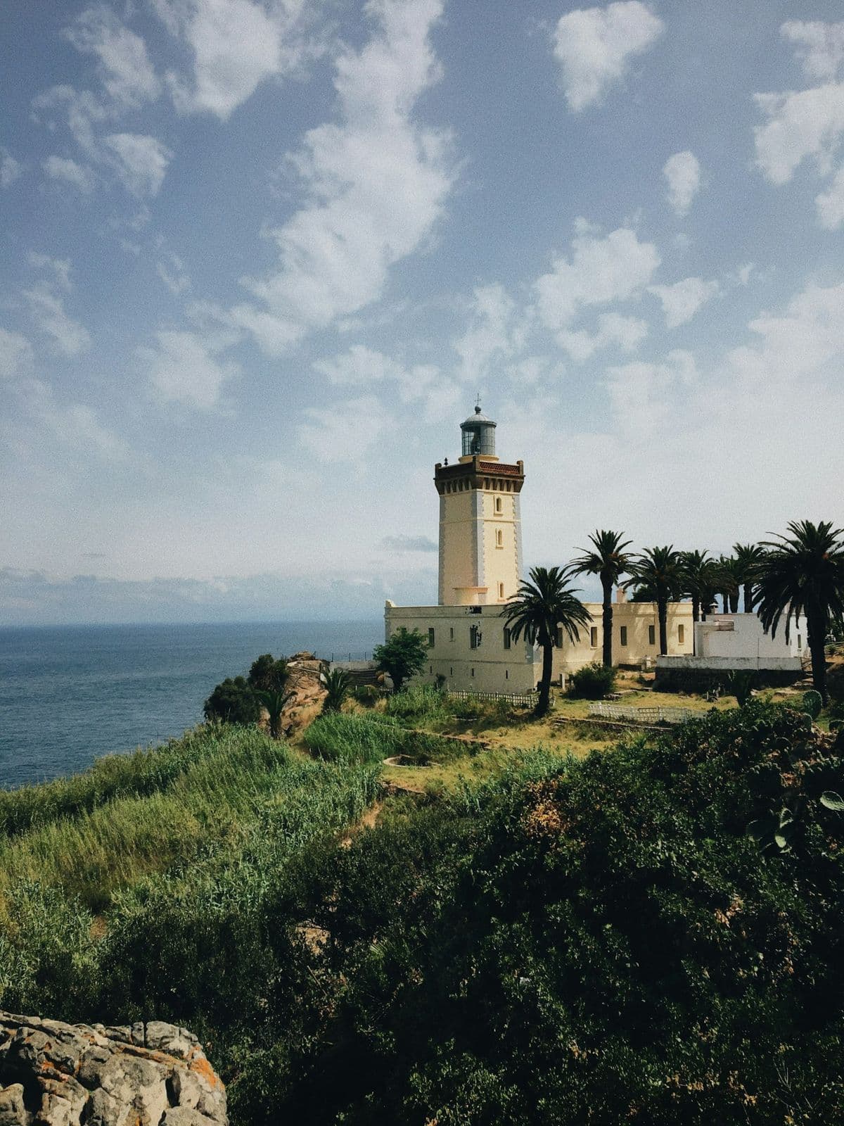Le phare du Cap Spartel, tour claire entourée de palmiers, au-dessus de la mer et de la végétation du cap