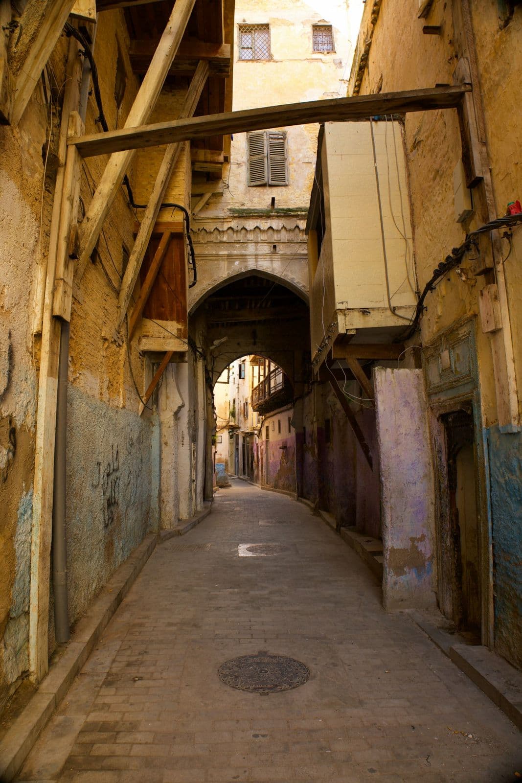 Ruelle pavée d'une médina marocaine, murs étayés par des poutres en bois et passage voûté au fond