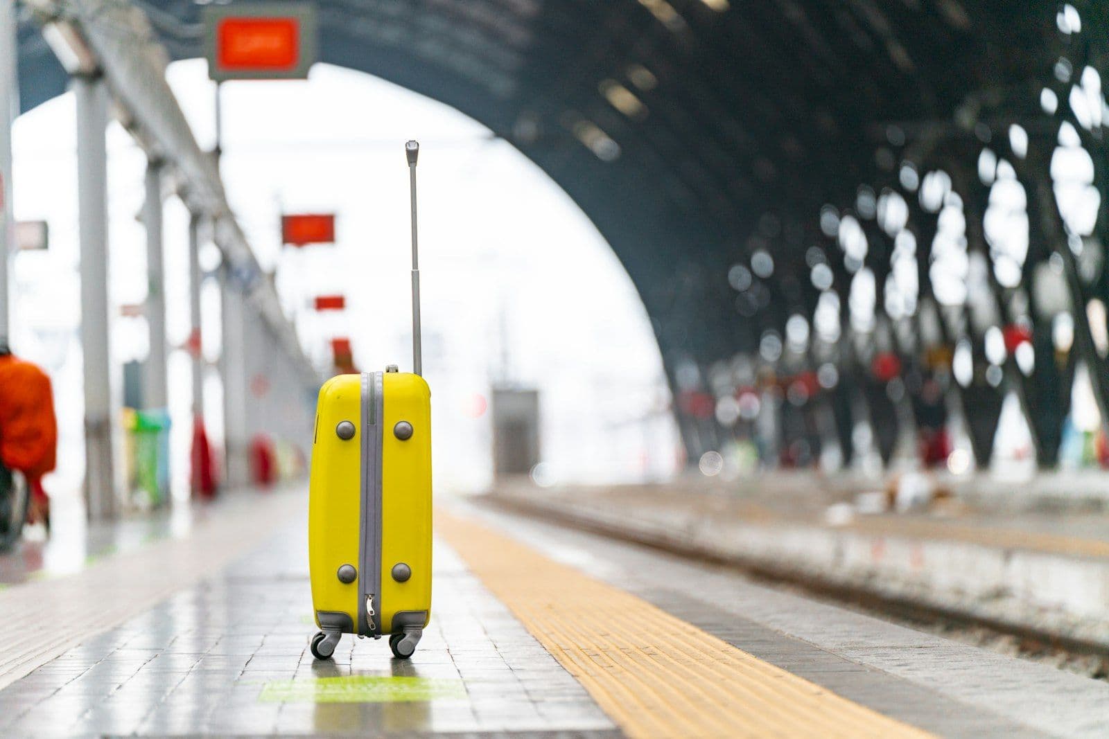 Valise jaune posée sur un quai de gare, sous une grande verrière