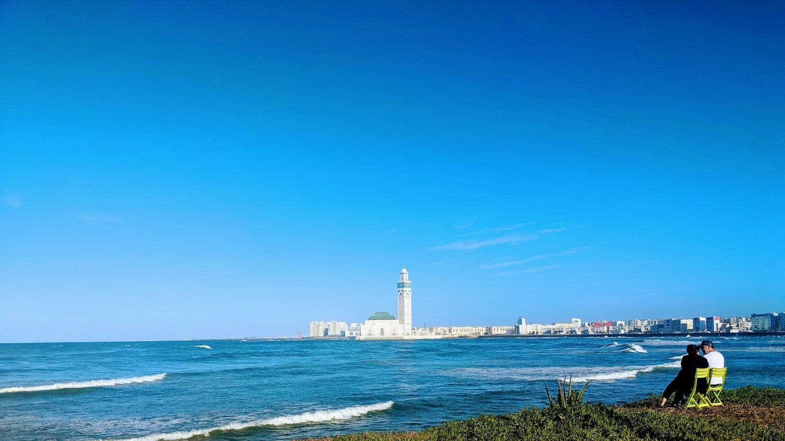 La mosquée Hassan II et son minaret vus de l'autre côté de la baie, avec l'océan et des vagues au premier plan, à Casablanca