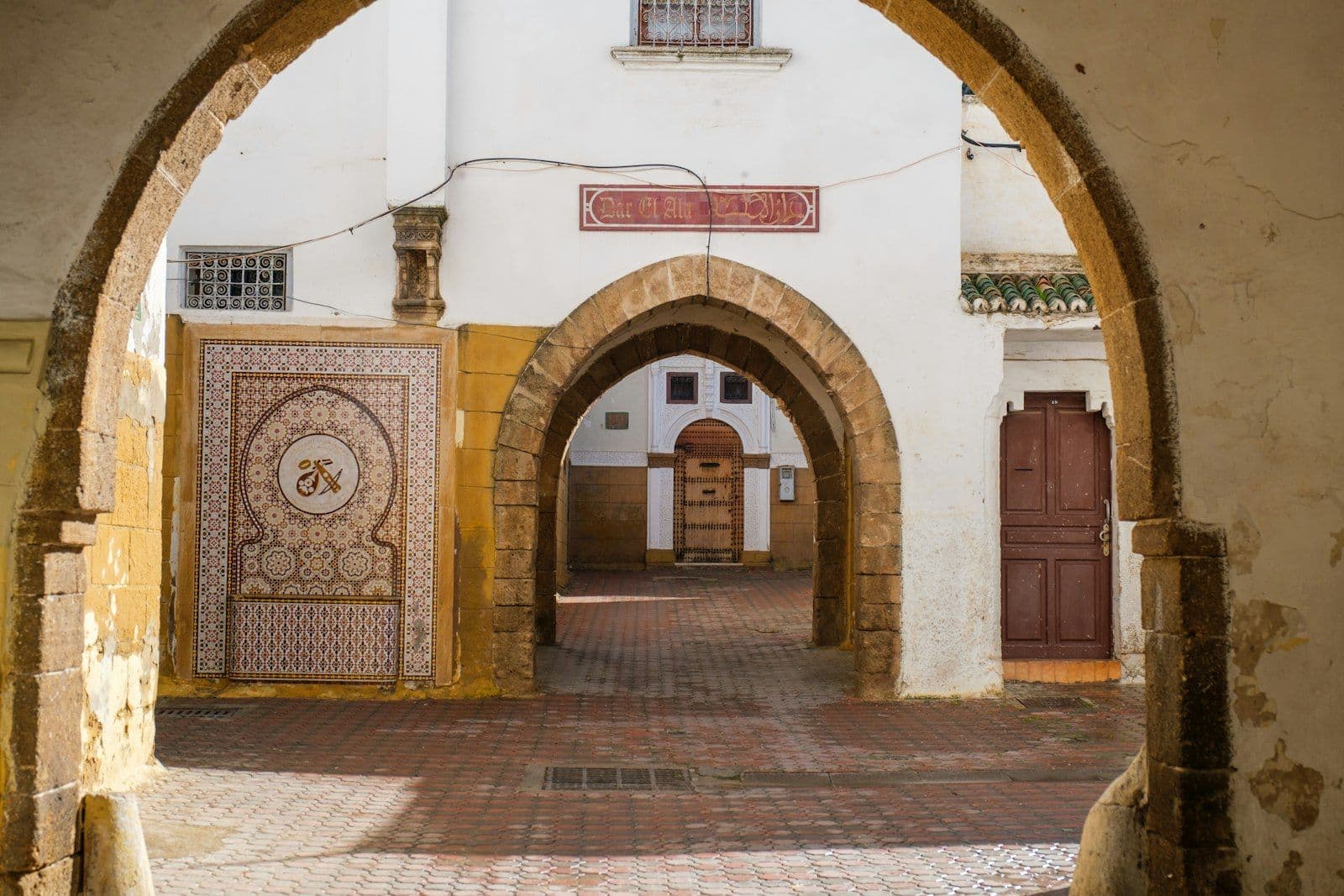 Arcades en pierre devant Dar Al Ala, dans le quartier des Habous à Casablanca, avec un panneau de zellige et des portes en bois