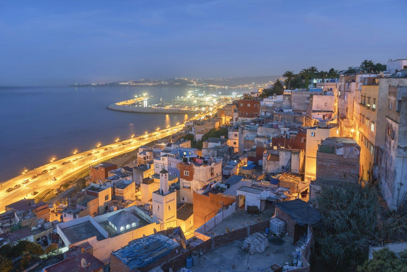 Tanger à la tombée de la nuit : toits de la médina au premier plan, port et avenue de la baie illuminée en arrière-plan