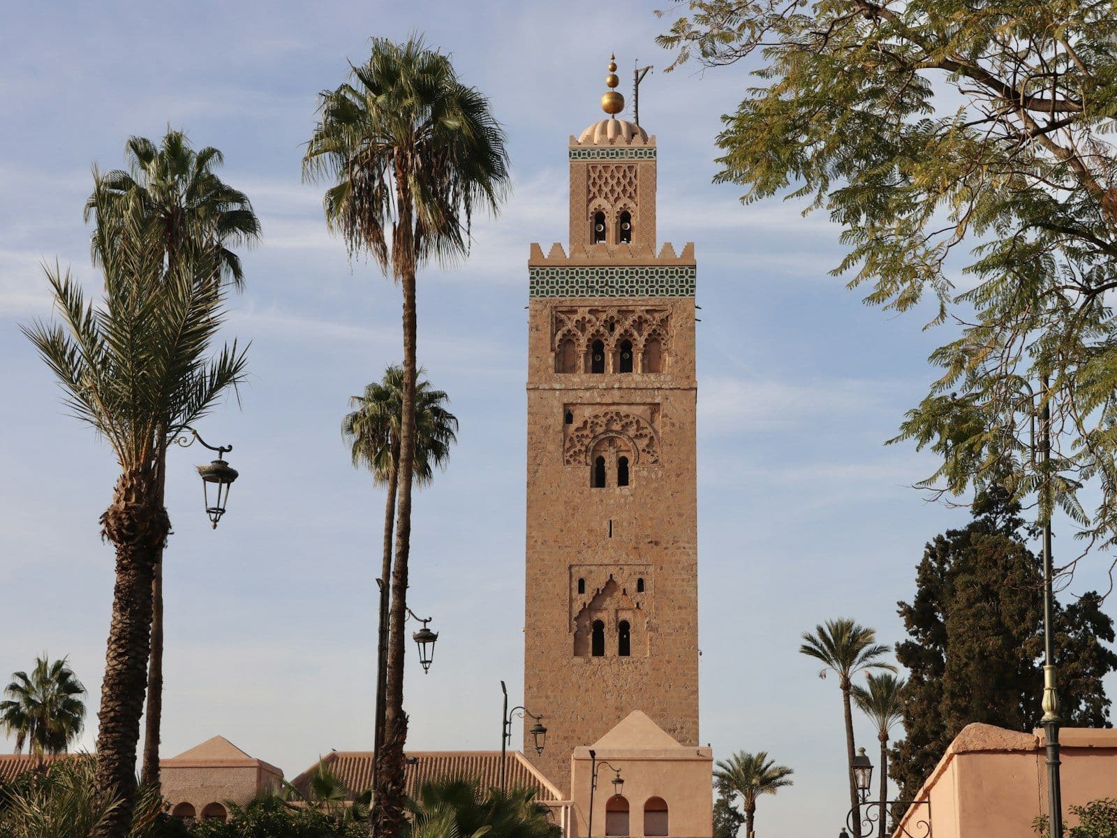 Le minaret de la Koutoubia à Marrakech entre des palmiers et des lampadaires, sous un ciel bleu voilé (photo d'illustration, la foire se tient à La Mamounia, non loin)