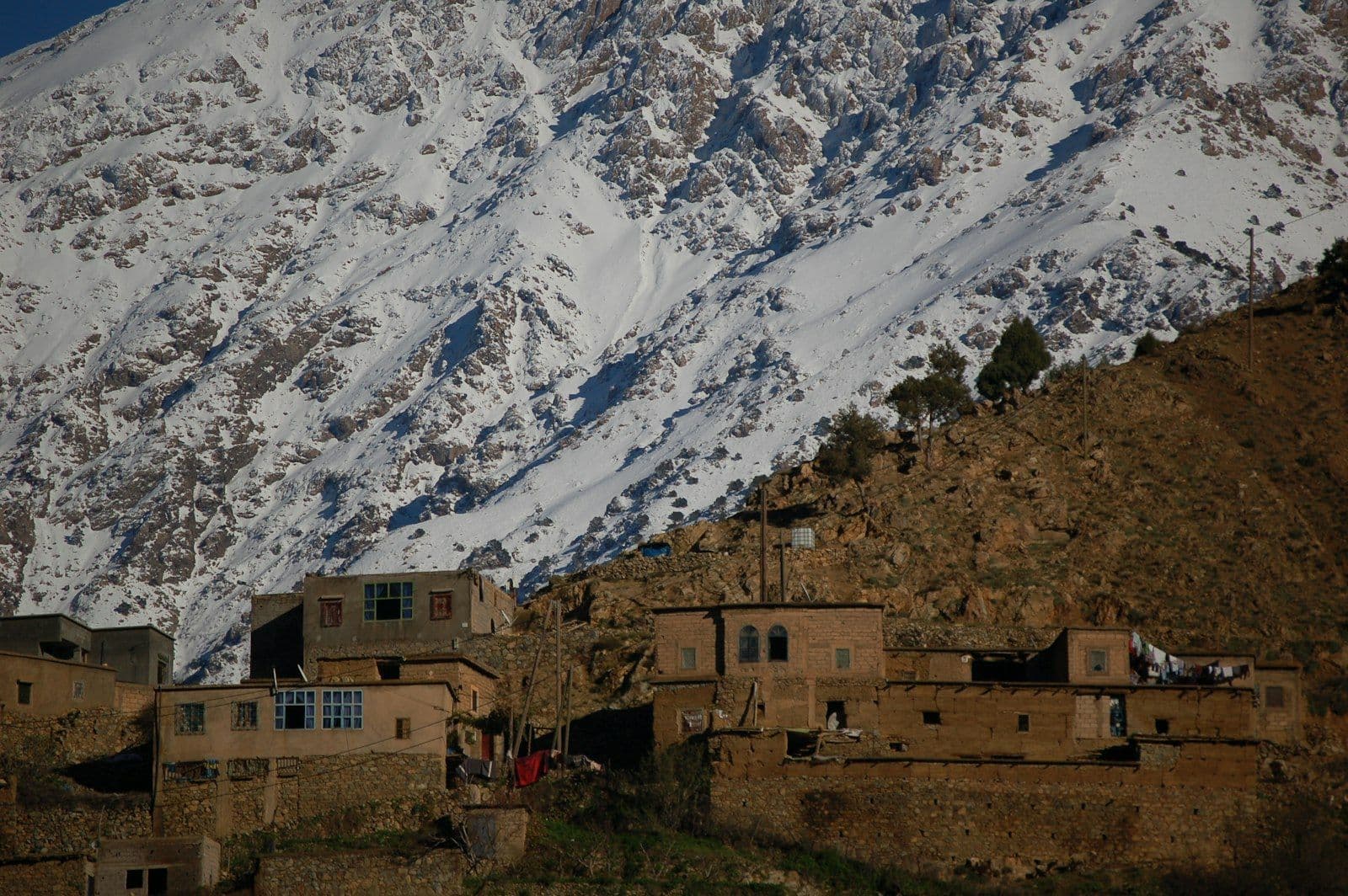 Maisons de pierre et de terre d'un village de montagne au pied d'un versant enneigé