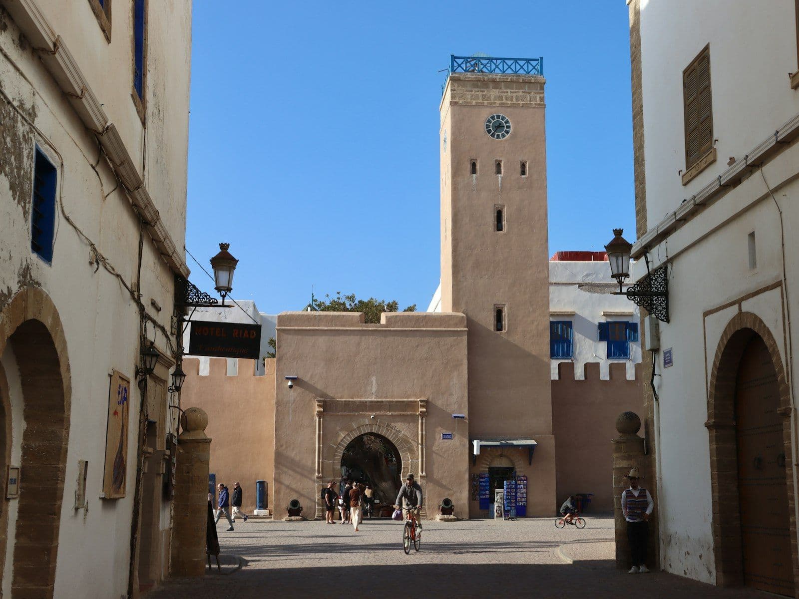 Tour de l'horloge à l'entrée de la médina d'Essaouira, sous un ciel bleu, avec des passants sur la place