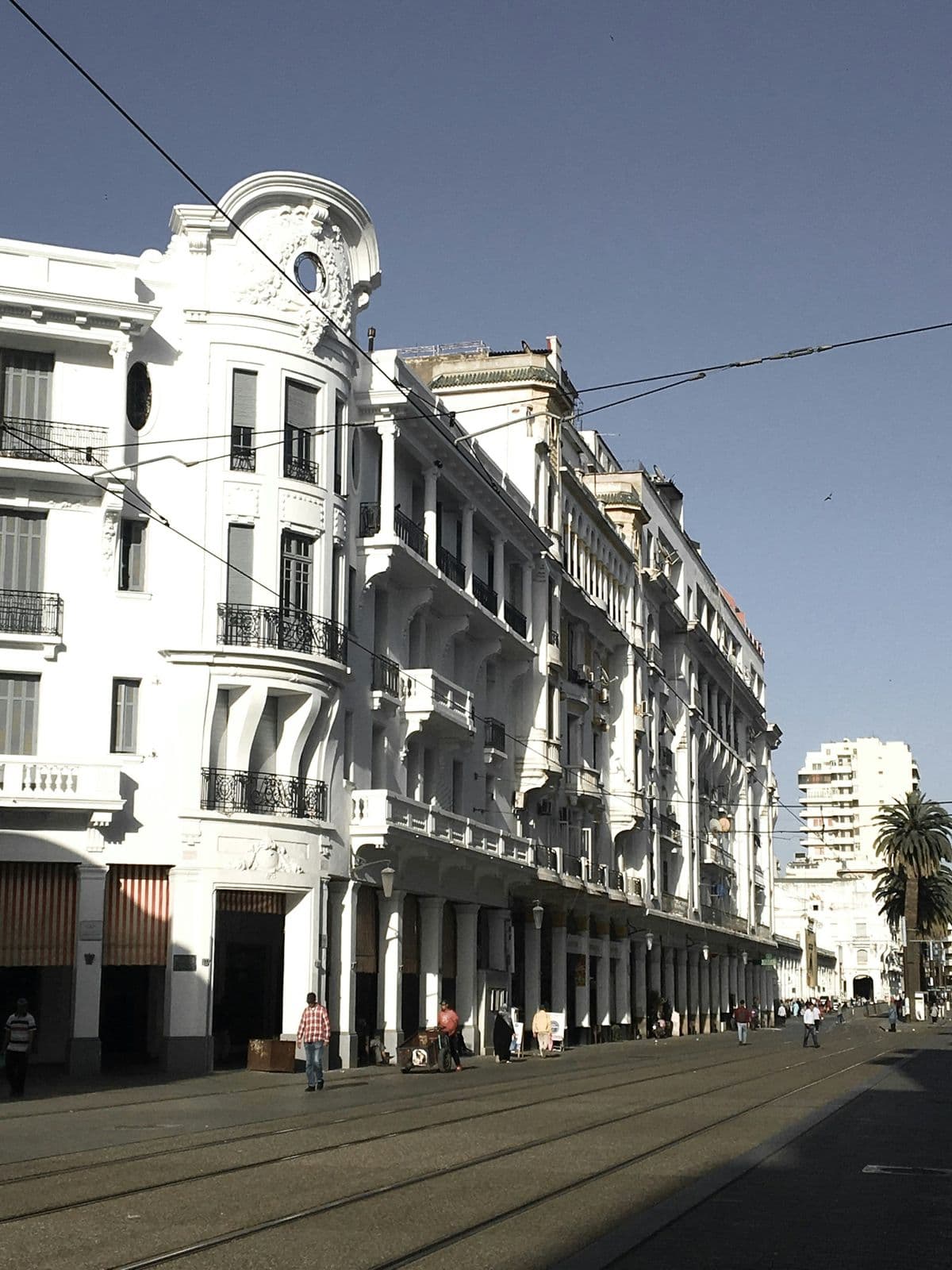 Immeubles blancs de style colonial avec balcons en fer forgé et rails du tramway dans le centre de Casablanca, sous un ciel bleu